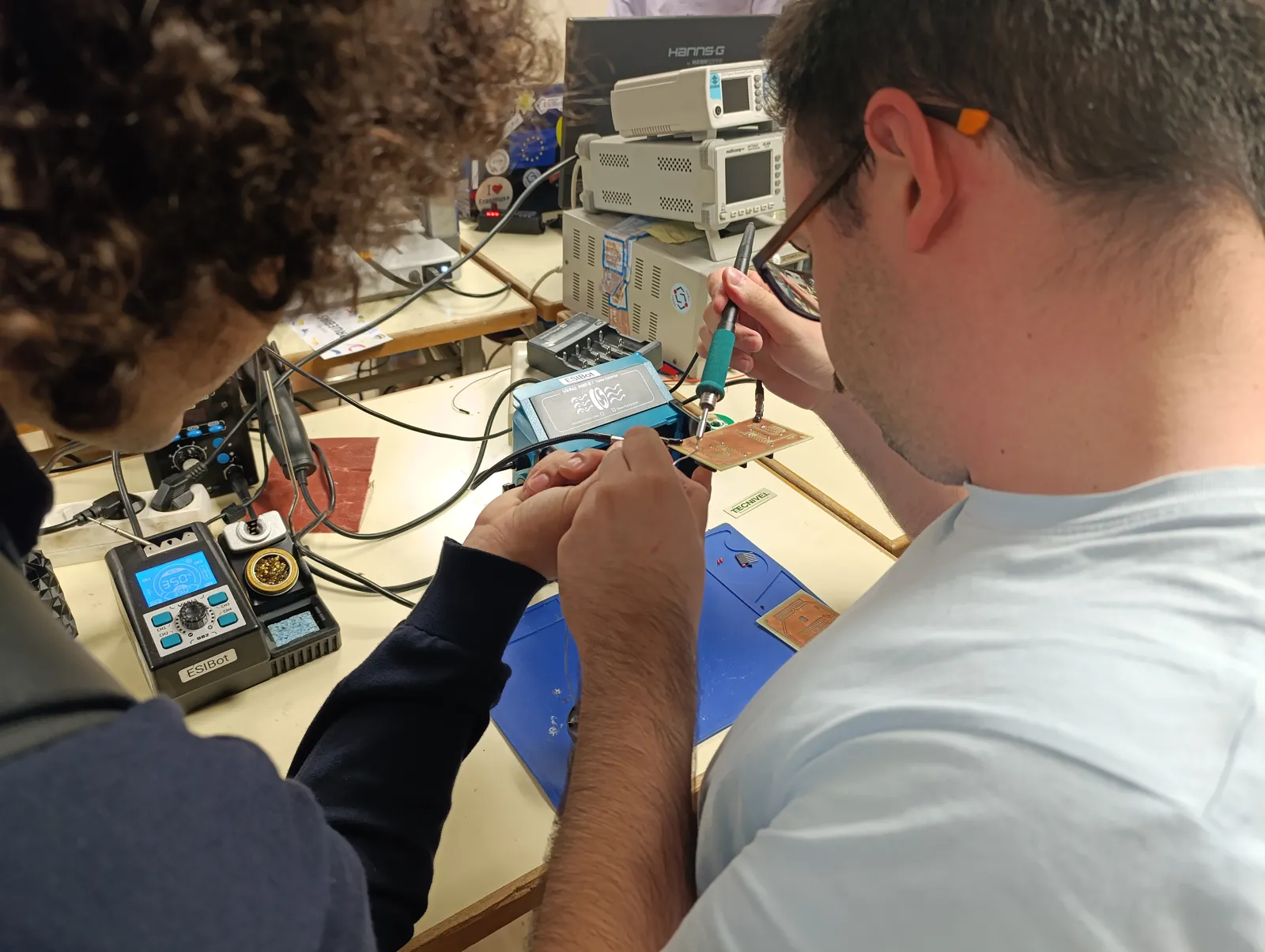 Dos estudiantes soldando una placa en el taller de ESIBot
